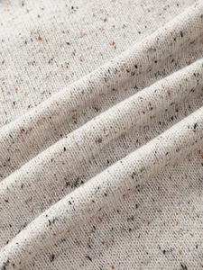Macro shot of soft tweed knit fabric featuring colorful orange and black fiber flecks