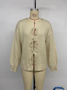 Detail der cremefarbenen Strickjacke mit drei Frontschleifen und Rippstrickbündchen