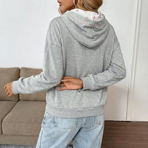Chic women's grey hoodie with pink floral lining and bow detail in a cozy home setting