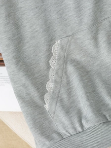 Detail of grey knitted hoodie showing floral lace trim on the pocket and ribbed hem
