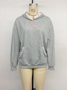 Detail of grey hoodie with white lace trim on hood and pocket featuring a pink bow design