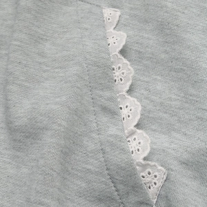 Close-up of grey sweatshirt fabric with detailed white floral lace trim and stitching