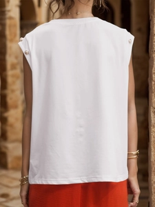 Close-up of a white sleeveless T-shirt featuring decorative gold buttons on shoulders