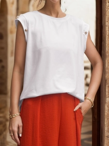 Close-up of white sleeveless top featuring decorative gold shoulder buttons and red pants