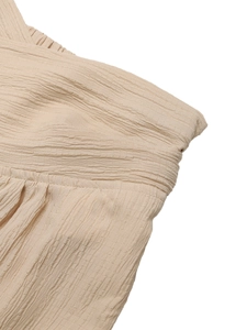 Detail of pleated fabric texture and crisscross neckline on beige high waist pants