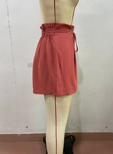 Detailed side view of high-waisted coral shorts featuring ruffled elastic waistband and belt