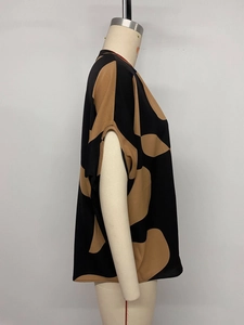 Detail view of women's loose V-neck shirt with abstract brown polka dots on black fabric