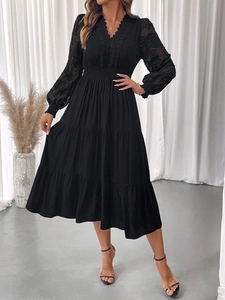 Detail of elegant black V-neck dress featuring sheer lace sleeves and tiered cake skirt