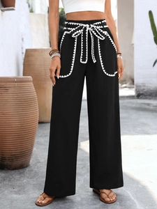 Detail of high-waist black trousers with white crochet lace trim and drawstring waist