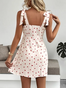 Detail of white mini dress featuring red heart prints and adjustable bow straps on the back