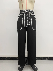 Detail of high-waist black wide-leg pants featuring contrast white wavy lace trim and belt