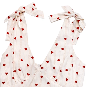 Detail of V-neck white summer dress with red heart print and tie-up ribbon shoulder straps
