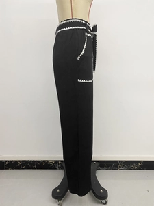 Detail view of high waist black trousers featuring white scalloped lace edges and side pocket