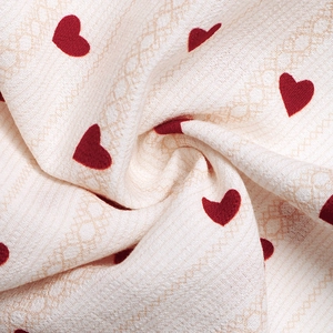 Detail of soft cream fabric with textured diamond grid and small red heart patterns
