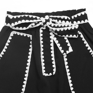 Detail of high waist trousers with black fabric, bow belt and white zigzag lace trim
