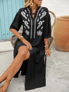Detail of white floral embroidery and V-neckline with tassels on a black bohemian dress