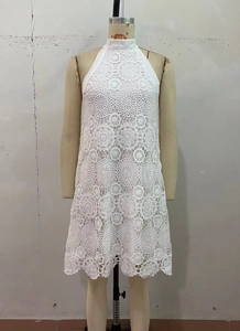 Detail of white crochet halter dress featuring intricate floral lace and scalloped hemline