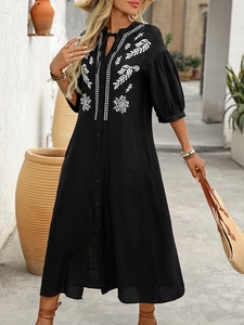 Close-up of bohemian black midi dress featuring white floral embroidery and V-neck tie detail
