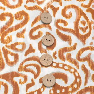 Nahaufnahme von Holzknöpfen auf weißem Kleid mit orangefarbenem Ikat-Paisleymuster