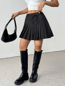 Detail of high-waisted black pleated mini skirt featuring adjustable side drawstring ties