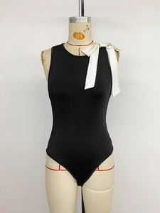 Détail d'un body noir sans manches avec un grand nœud contrasté crème sur l'épaule gauche