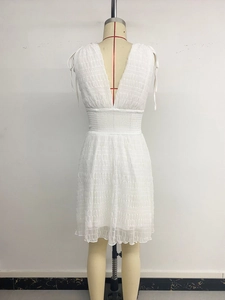Detailed view of white sleeveless V-neck dress with smocked waist and ruffled hem texture