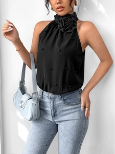 Detail of black halter top featuring 3D floral accent and pearl embellishments on the neckline