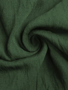 Gros plan détaillé du tissu crêpe vert foncé montrant le grain texturé et le drapé doux