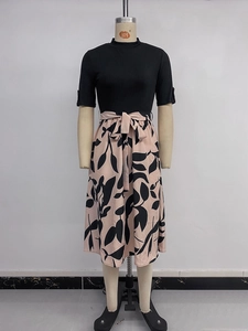 Détail du haut en maille noire et jupe midi rose à fleurs avec ceinture nouée à la taille
