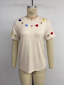Détail de broderie de cœur colorée et découpes sur un T-shirt rose à manches courtes