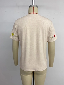 Détail des manches du t-shirt abricot avec broderies de cœurs colorés et designs ajourés