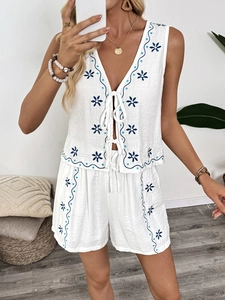Détail d'un ensemble d'été blanc deux pièces avec broderie florale bleue et bords ondulés