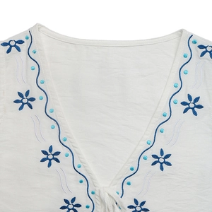 Vue détaillée du col en V avec broderie florale ethnique bleue sur un tissu blanc doux
