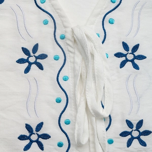 Détail du chemisier ethnique blanc avec broderie florale bleue et cordon de serrage au col