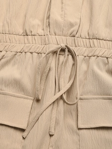 Detail of drawstring waist and cargo pockets on light brown textured jumpsuit fabric
