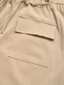 Detail of light beige textured fabric jumpsuit with elastic drawstring waist and pocket