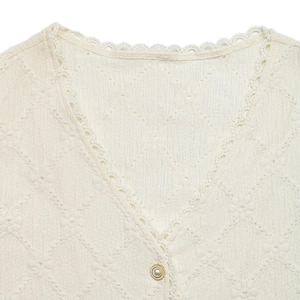 Close-up of V-neck lace trim and decorative pearl button on ivory knit top shirt