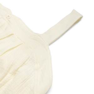 Détail de la combinaison en coton texturé crème montrant la fine bretelle et le bouton