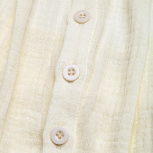 Gros plan sur le tissu beige texturé et boutons blancs d'une combinaison d'été fluide