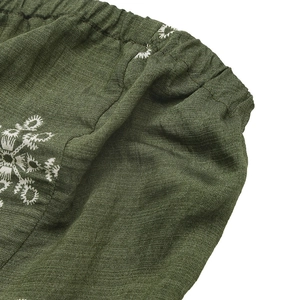 Detail of green summer jumpsuit featuring elastic waistband and white floral embroidery