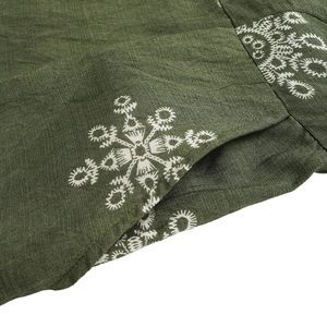 Detailed view of white snowflake embroidery and pocket stitching on dark green linen fabric