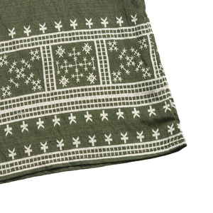 Close-up of olive green linen fabric with white ethnic geometric embroidery and stitching