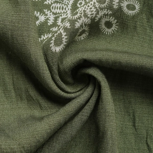 Detailed close-up of dark green linen fabric with white floral embroidery and texture