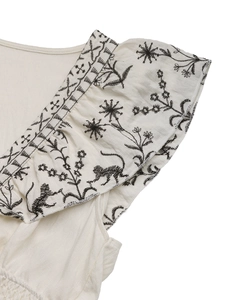 Detail der cremefarbenen Bluse mit schwarzer Affen- und Blumenstickerei und Rüschen