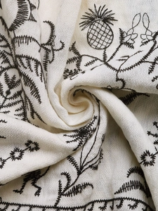 Nahaufnahme von cremefarbenem Textil mit detaillierter schwarzer Ananas- und Blumenstickerei