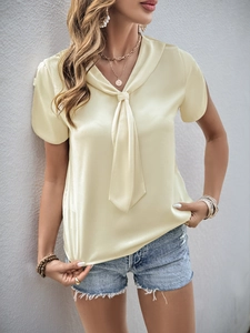 Detailed texture of light yellow satin short sleeve top with elegant scarf tie neckline