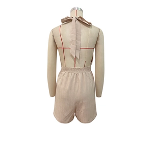 Back view of beige halter jumpsuit featuring open back and elastic pleated waist detail