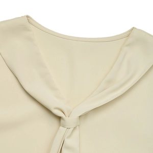 Detail of the V-neckline and decorative knot on cream sleeveless chiffon blouse