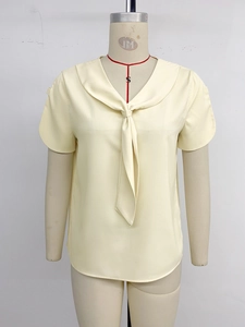 Detail of elegant pale yellow short sleeve shirt featuring V-neckline and stylish scarf tie