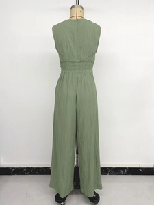 Detail of sage green sleeveless jumpsuit showing elastic waist smocking and textured fabric